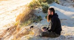 a man sitting on sand with a dog