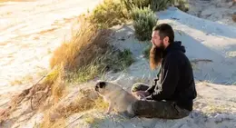 a man sitting on sand with a dog