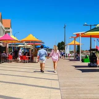 a man and woman holding hands walking down a boardwalk with colorful umbrellas