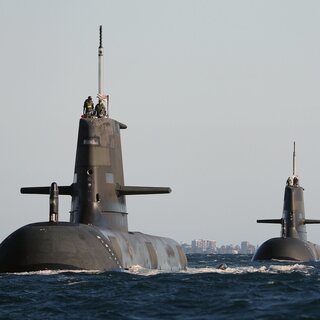 Three naval submarines travelling on the ocean surface in formation.