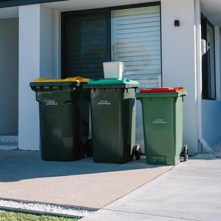 Three household bins with different coloured lids placed on a driveway outside a residential home for collection.
