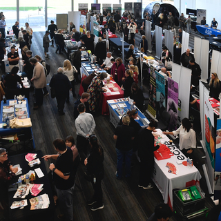 Crowded indoor Rockingham Jobs Fair with job seekers engaging with exhibitors at information stalls.