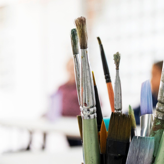 Paint brushes in focus with an art workshop taking place in the Rockingham Arts Centre multipurpose room in the background.