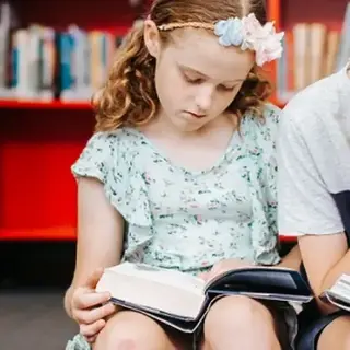 Two children sitting together in a library reading books.