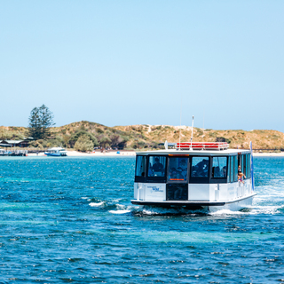 Passenger ferry travelling across clear blue water with sandy dunes and shoreline in the background.