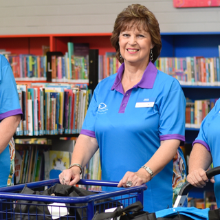 Three library volunteers in uniform standing with book trolleys.