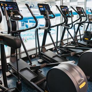 Row of cardio machines overlooking an indoor pool, with people using the equipment.