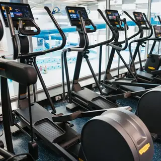 Row of cardio machines overlooking an indoor pool, with people using the equipment.