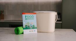 FOGO kitchen caddy bin with a roll of caddy liners and a booklet.