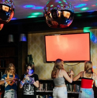 Teens gathered in a library space with bookshelves and colourful disco lights during a library event.