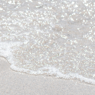 White organic shaped sculpture at the beach on the sand with lapping waves.