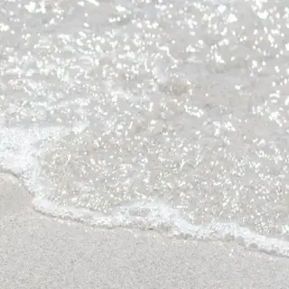 White organic shaped sculpture at the beach on the sand with lapping waves.