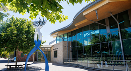 Exterior of the Mary Davies Library and Community Centre with large windows, trees, and a blue-and-white sculpture out front.