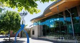 Exterior of the Mary Davies Library and Community Centre with large windows, trees, and a blue-and-white sculpture out front.