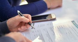 Hands holding a pen while filling out a form on a table.