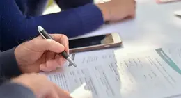 Hands holding a pen while filling out a form on a table.