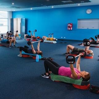 Participants taking part in a group fitness class, lifting weights while lying on mats in an indoor fitness studio.