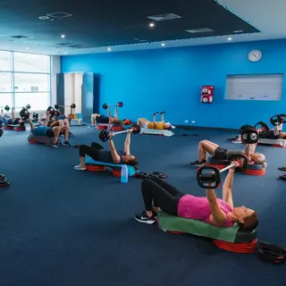 Participants taking part in a group fitness class, lifting weights while lying on mats in an indoor fitness studio.
