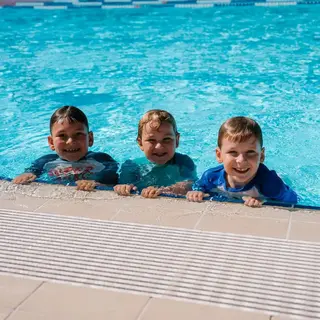 Three children holding onto the edge of an outdoor swimming pool during a swim session.
