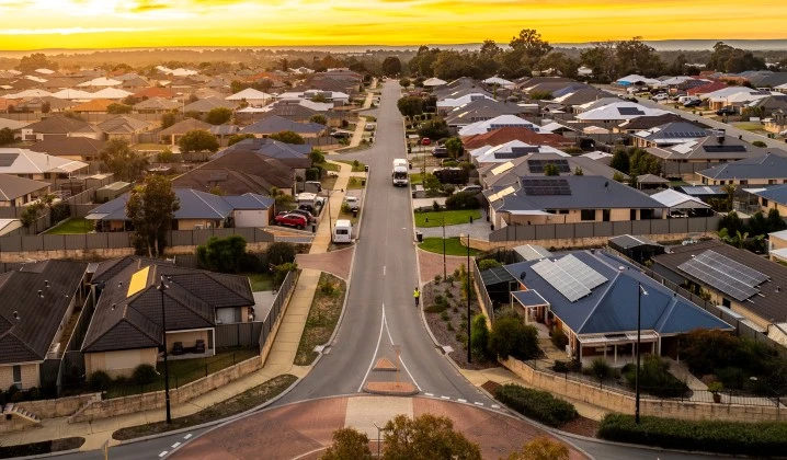 Aerial view of a suburban residential neighborhood at sunset, with a straight two-lane road running through the center. 
