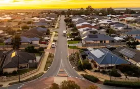 Aerial view of a suburban residential neighborhood at sunset, with a straight two-lane road running through the center. 