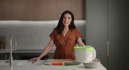 a woman standing in front of a counter with a bucket of vegetables
