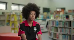 a boy with curly hair sitting in a room with books