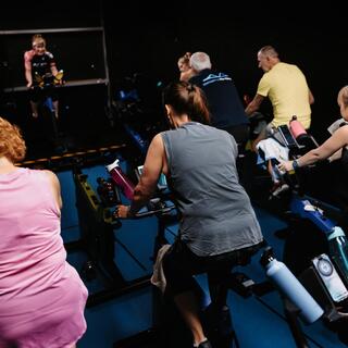 People taking part in an indoor spin class, riding stationary bikes in a dark fitness studio.