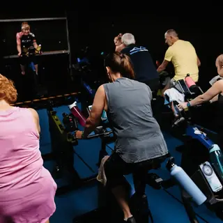 People taking part in an indoor spin class, riding stationary bikes in a dark fitness studio.