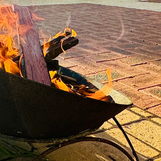A smoking ceremony fire burning in a metal bowl with green leaves beside it on paved ground