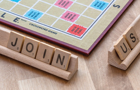 Scrabble board and Scrabble letters spelling out 'join us'
